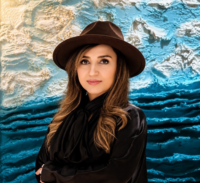 Hanieh M. Bagher in front of a textured ocean-blue painting
